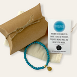 Turquoise beaded bracelet with a gold charm on a white background, accompanied by a brown pillow box and information card.